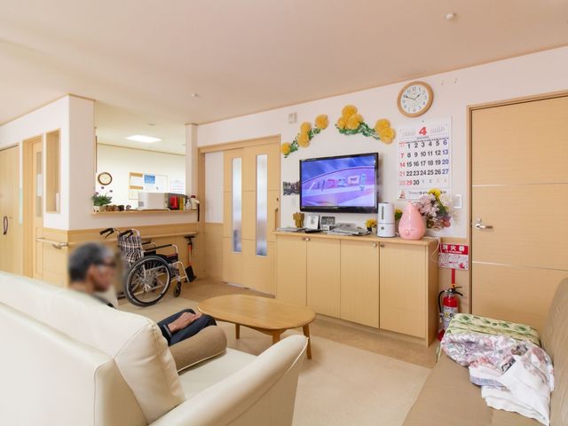 居心地の良いリビング空間 食堂 ソファに座りリラックスする方々、共有するリビングは温もり溢れる時間を提供します。週間カレンダーや時計があり、日常生活のリズムを大切にできる環境です。