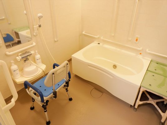 水はけの良い床材を使用した浴室。洗い場にはシャワー椅子があり、浴槽の横には腰を掛ける台が置かれている。