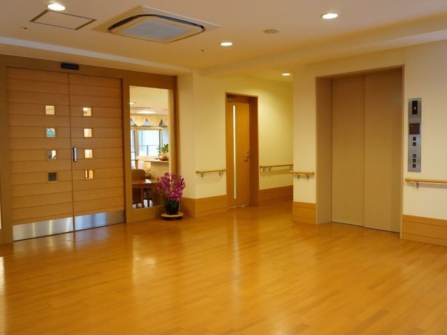 廊下と扉の様子 廊下 広々とした廊下には落ち着いた色合いの木目が美しく、スタッフと利用者の円滑な移動を支えています。