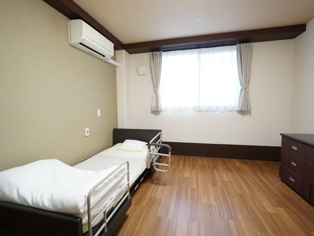 落ち着いた色合いの居室 居室 ゆったりとした床のスペースがあり、ベッド周りもすっきりと配され、日中の陽光が差し込む心地よい個室です。ケアに従事される方にも、過ごしやすい環境が整っています。