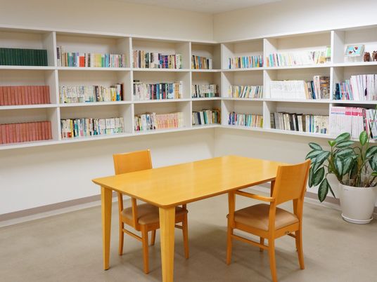 グループホームには図書室があり、さまざまな書籍が本棚に並べられている。またフロアには、テーブルと椅子が置かれている。
