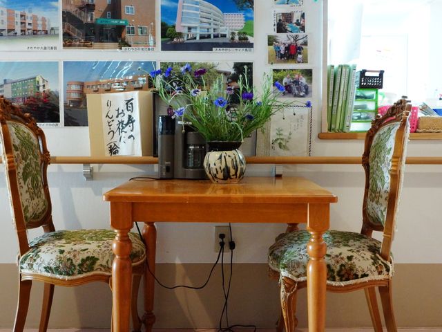 休憩コーナーの花とテーブル コーヒーメーカー くつろぎの時間を演出するロビーには、華やかな花が飾られ、温かみのある雰囲気を醸し出しています。ここでのひとときは、日々の憩いの場となります。