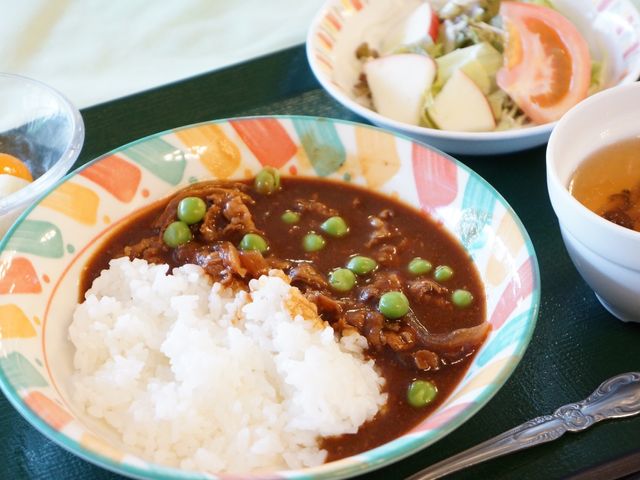 カレーライスとサラダの食事 食事 色とりどりの食器に盛られたカレーライスは、彩りも考えられたバランスの良い食事です。栄養面への配慮が見て取れる献立が、利用者様の健康を支えます。