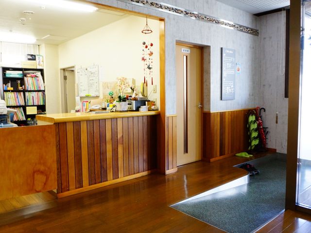 受付と廊下のエリア 受付カウンター 心地よいフロントが訪問者をお出迎えし、安らぎとくつろぎを提供する空間です。木目調のインテリアが温かみを感じさせます。