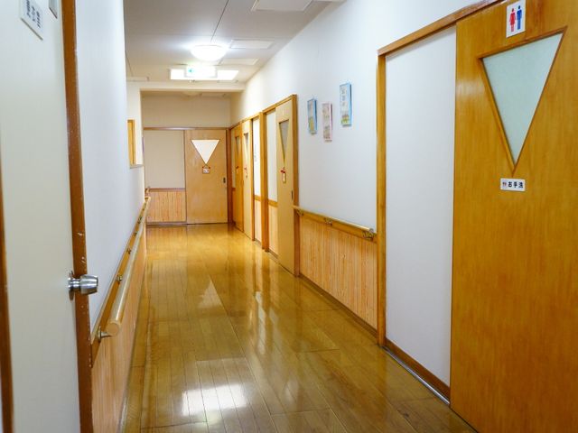 温もりある廊下 トイレ入り口の周辺 手すりが設置された清潔感のある廊下です。壁には掲示物もあり、明るい雰囲気が感じられます。