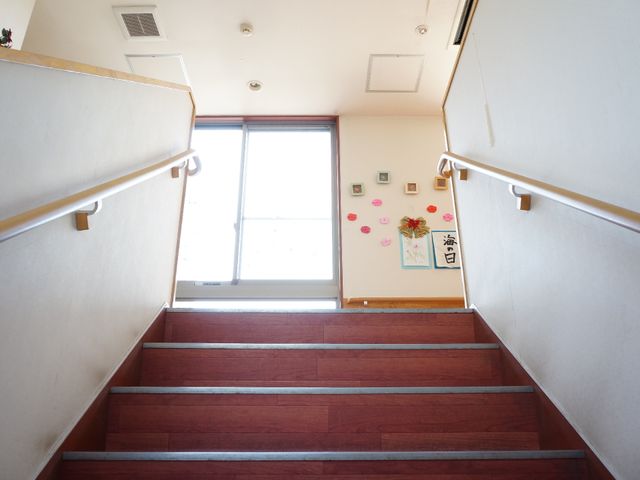 玄関階段と掲示物 階段 手すり付きの階段は明るく、壁には小さな掲示物があり温かみのある空間を形作っています。ここを通ることで、日々の通路が安全かつ快適になっています。
