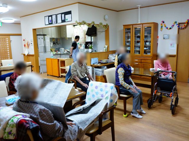 共有空間で過ごす人々 リビング2 暖かい雰囲気のダイニングルームで、利用者の方々が憩いの時を過ごされています。スタッフの方が優しく対応されており、安心してご利用いただける環境です。