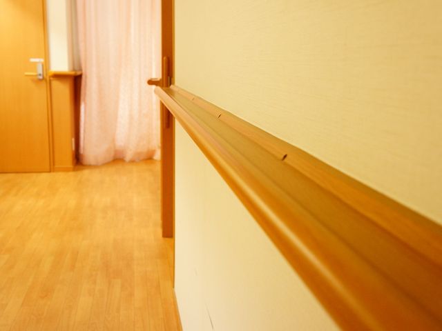 廊下の手摺と木目調の扉 私室手すり 手すり沿いの暖かみのある木目調の廊下です。安全に配慮された設計で、働く環境も快適です。