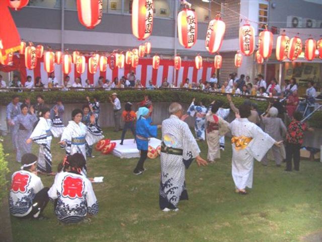盆踊りを楽しむ人々 夏祭り 提灯で飾られた庭で地域の方々と共に盆踊りを楽しむ様子です。和気あいあいとした雰囲気の中で、様々な世代が交流を深めています。