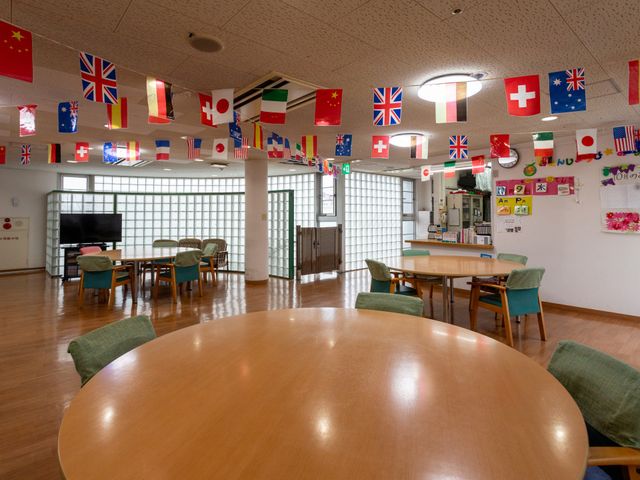 明るい飾り付けの部屋 ダイニングルーム 天井からカラフルな旗が飾られた明るい空間で、テーブルや椅子が整然と配置されています。