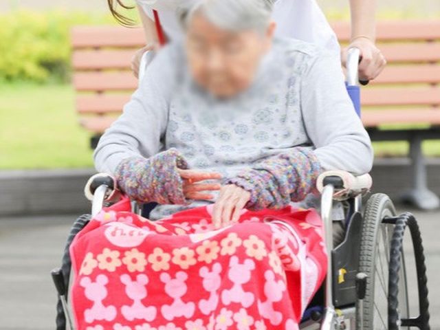 介護中庭 中庭 中庭でスタッフが車椅子の利用者をサポートしています。心温まるひと時を過ごせます。