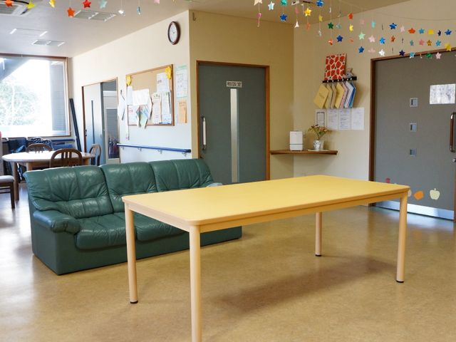 広々とした共有ラウンジ 居間 落ち着いた色合いのゆったりとしたソファが配置された共有スペースです。壁に飾られた手作りの装飾品がアットホームな雰囲気を演出しています。