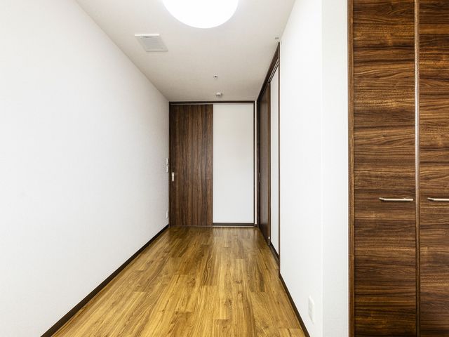 居室の木製ドアとベッド 居室 温かみのある木目調のドアが特徴的な居室です。シンプルで清潔感のある空間が、快適な生活を支えます。