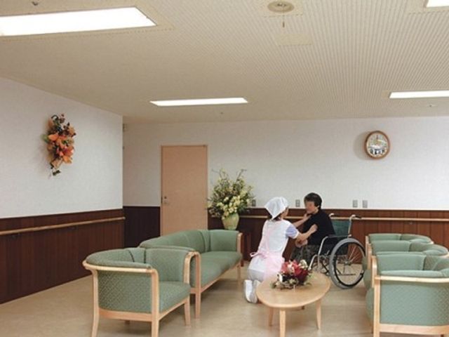 快適なラウンジの一角 ホール 広々としたラウンジでは、スタッフが利用者様と優しい対話をしています。ゆったりとした空間で、心地よい交流の時間を過ごせる場所です。