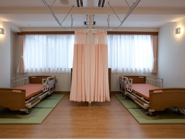窓際にベッドがある居室 居室   自然光が差し込む静かな空間です。カーテンで仕切られたプライベートスペースも備えています。