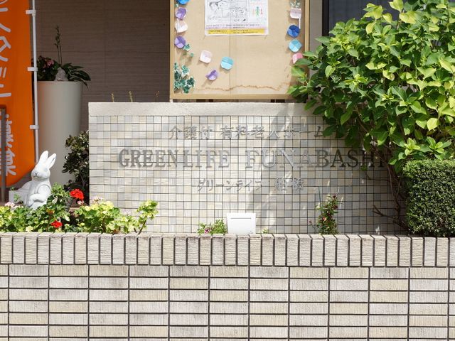 施設の外にある看板 表札 温かみのある花と緑に囲まれた看板が目を引きます。スタッフの温もりが感じられる環境での仕事に、心惹かれる方も多いでしょう。