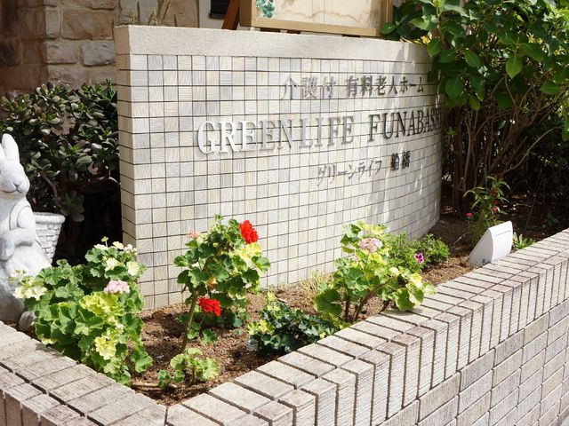 花壇付きの明るい看板 表札 清潔感のあふれる看板が、新緑と花々に囲まれています。皆様のお越しをお待ちしております。