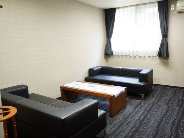 落ち着いた色の居室 応接室 広々とした居室で、シックな色合いの家具が設置されており、くつろぎやすい雰囲気が感じられます。窓からの自然光も柔らかく差し込んでいます。