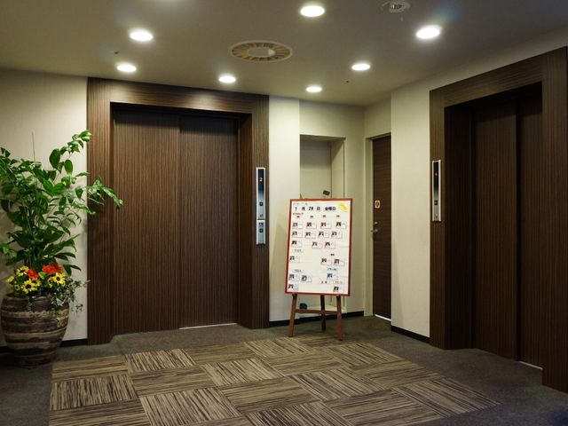 廊下と掲示物の静かな風景 エレベーター前 穏やかな色合いの廊下に、住居の方々の活動が案内されている掲示物が設置されており、ゆったりとした時間の流れを感じさせます。