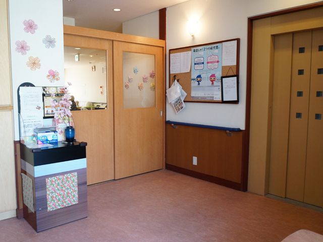 フロントと掲示板の一角 エレベーター 清潔感ある広々とした受付エリアです。情報発信の場として、多様な掲示物が整然と配置されています。