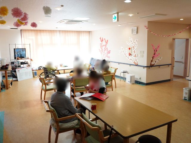 桜模様の壁画と共用スペース 居室 明るく広々とした共用スペースでは、壁に描かれた桜の壁画が心和ませます。利用者の方々が集い、憩いの時間を過ごす様子が伺えます。