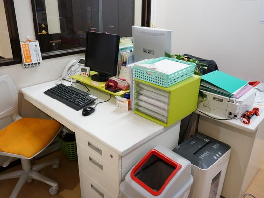 スタッフの事務所にあるデスクにはパソコンや電話、書類棚が置かれているが、きちんと整頓されている。デスクの横にはシュレッダーが置かれている。
