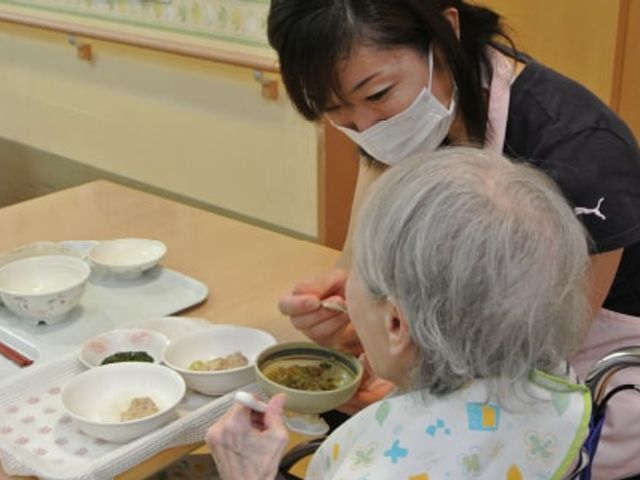 食事介助の様子 ダイニングルーム 職員がご入居者様の食事を丁寧にお手伝いしています。温かな交流の場となっています。