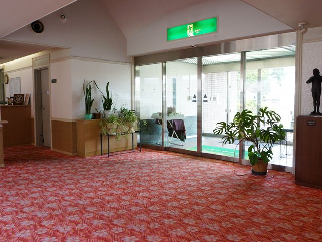 エントランスの快適空間 玄関ホール あたたかみのあるカーペットが敷かれたエントランスで、緑の植物が空間に彩りを添えています。明るく開放感のある出迎えが心を和ませてくれます。