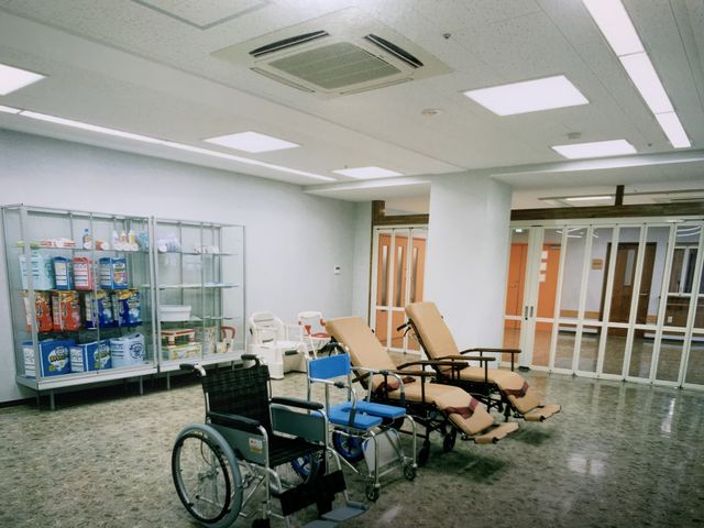 リハビリ用スペース 機能訓練室 明るい照明の下で、リハビリ用のベッドと車椅子が整然と配置されています。