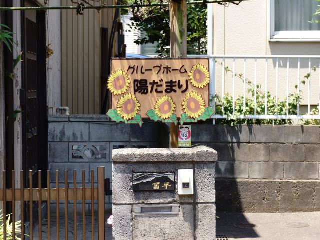 ひまわり看板の施設入口 玄関 明るく暖かい雰囲気のエントランスです。ひまわりの看板が来訪者を温かく迎え入れています。