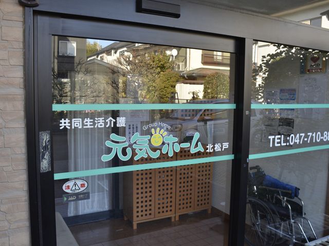 施設入り口 エントランス 車椅子でも楽に通れる幅広いエントランスが安心です。明るい笑顔のロゴが出迎えます。