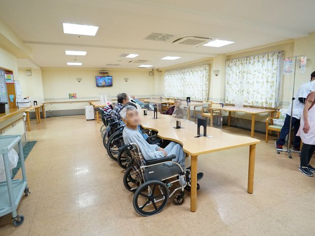 共有スペースでの様子 共有スペース ゆったりと配置されたテーブルと、明るい窓辺が印象的です。スタッフが利用者の方々のそばで丁寧にサポートをしています。