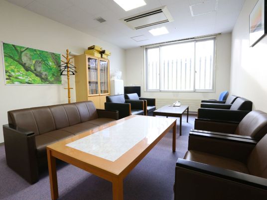 談話室はゆったりとしたスペースを設けおり、10名程度座れる黒と茶の革張りのソファが置かれている。壁には絵画が飾られている。