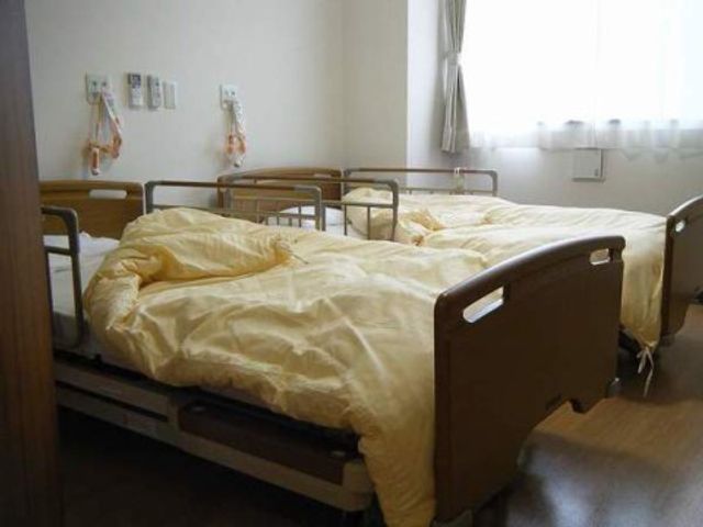 快適な居室の一角 二人部屋 ぬくもりを感じる居室で、掛け布団が整えられたベッドが並んでいます。日の光が差し込む心地よい空間です。