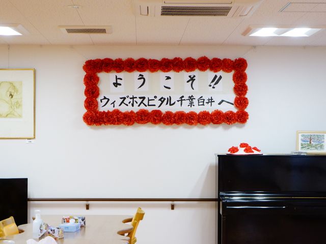 壁掛けのお祝い飾り ようこそ！ 壁には華やかな飾りがあり、温かく明るい雰囲気の共有スペースです。楽器もあり、レクリエーションでのひとときを想像しやすくなっています。