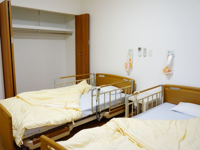 居室のベッドとクローゼット ベッド横のクローゼット きれいに整えられた居室は、リラックスして過ごせるよう配慮されています。個々のスペースが確保され、快適な生活を支援しています。