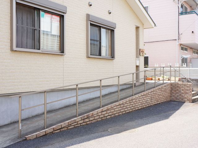 明るい外観の入り口 外観 手すり付きのスロープが設けられた入口は、どなたでも安心してご利用いただける設計です。余裕をもった空間は、明るく開放感があります。