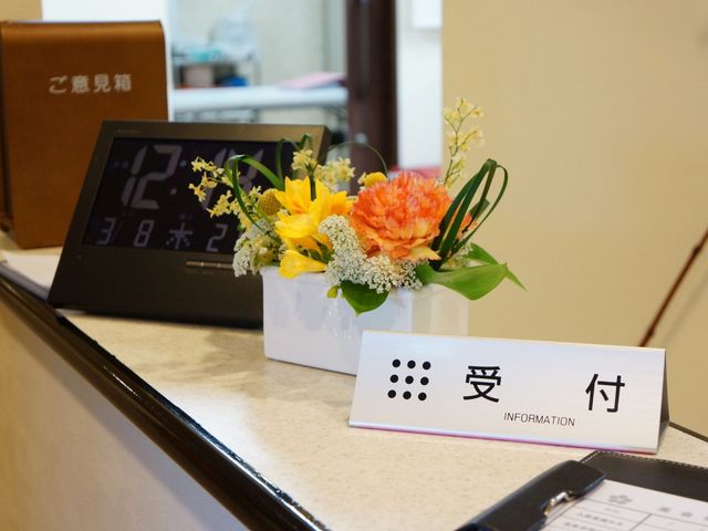 情報カウンターと花瓶 受付 落ち着いた雰囲気の受付に明るい色の生花が飾られており、訪れる皆様を温かく迎えます。