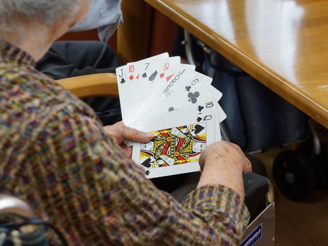 トランプを楽しむ高齢者 食堂・談話室 ゲームを通じてコミュニケーションが取れる温かな空間です。手元に集中する皆様の楽しいひと時をサポートしています。