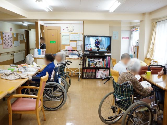 共有スペースの様子 食堂・談話室 ゆったりとした雰囲気の食堂で、利用者の方々がテレビを観ながらくつろいでいます。明るく開放的な空間で、コミュニケーションが育まれています。