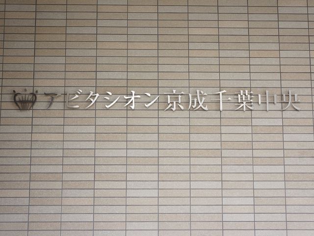 壁に掲示された看板 玄関 清潔感漂う外壁に印象的なロゴが目を引きます。ケアを通じて新しいキャリアを築いたい方に適した職場です。