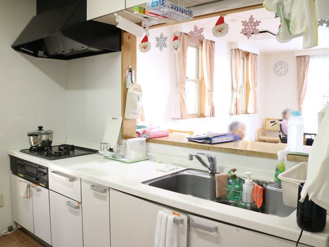 キッチン全景と利用者 キッチン 清潔感のあふれるキッチンスペースで、利用者さまが家庭的な環境で食事の準備をしている様子です。