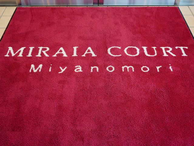 エントランスのロゴ入りマット 入り口カーペット 赤い色彩が鮮やかなエントランスのマットには、温かみのある歓迎の文字が映えています。