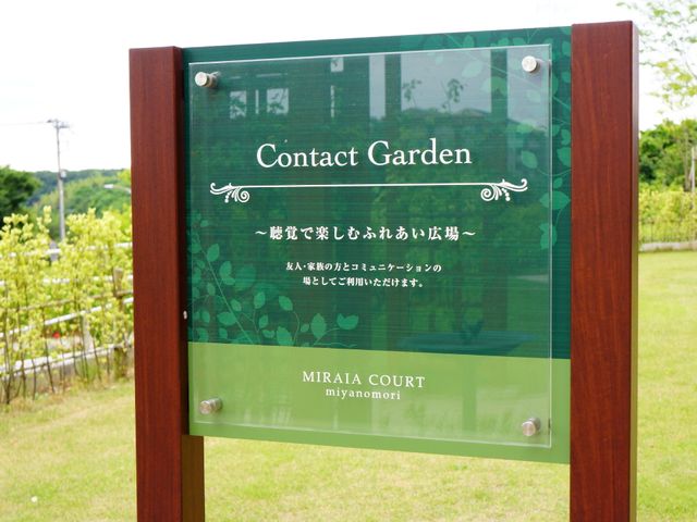 緑に囲まれた看板 ふれあい広場 緑豊かなガーデンを望む看板が、来訪者を優しい風景へと誘います。日々の憩いに最適な空間がこちらです。