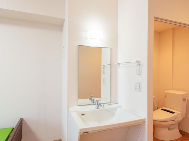 居室洗面台 お部屋には、毎日の身だしなみを整えやすいよう、大きな鏡付きの洗面台を設置。車いすの方でも使いやすいよう、足元にはスペースを空けております。