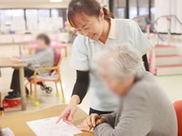 和やかな雰囲気の場面 リビング 明るい自然光が差し込むリビングでは、スタッフが利用者に丁寧に説明をしています。