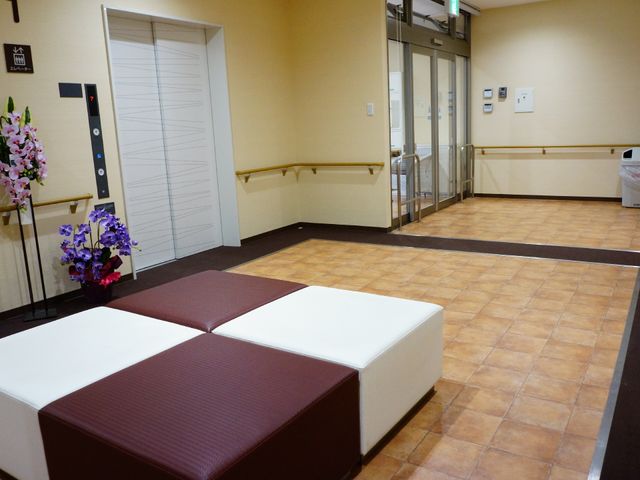 エレベーター前の休憩スペース エントランス 広々としたロビーには、ゆったり座れるベンチが配置されており、待ち時間も快適にお過ごしいただけます。