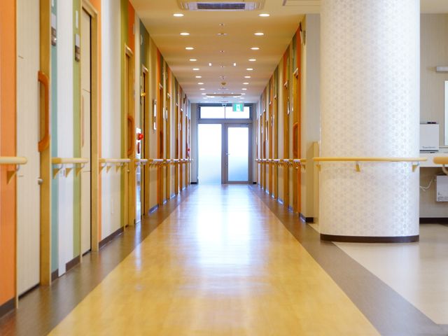 廊下の端末景 施設内廊下 手すりが設置された明るく清潔な廊下を備え、安心して歩行が行える設計です。ゆったりとした空間が広がる通路からは、心地よい環境づくりに配慮されている様子がうかがえます。