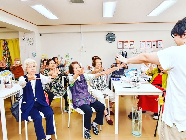 元気な様子の多目的室 活気に満ちた多目的室で、笑顔と振り付けを交えたレクリエーションが行われています。軽快な音楽に合わせて、参加者は楽しそうに体を動かしていらっしゃいます。