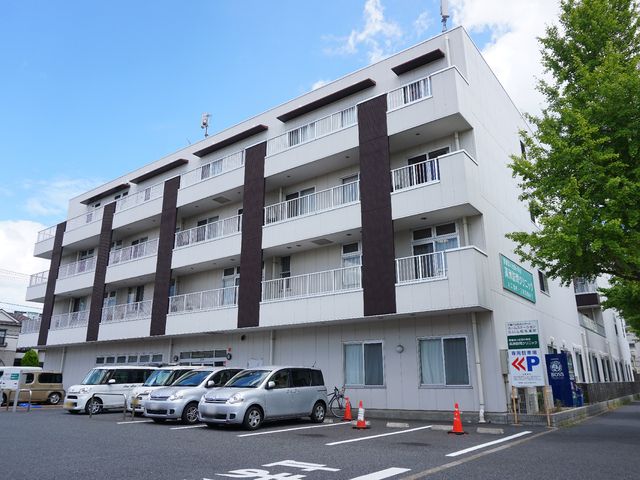 白と茶色の建物エクステリア 外観 ゆとりある駐車スペースが備わった、清潔感のある白い建物です。日当たりも良く、心地よい環境でお過ごしいただけます。